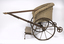 A twin push chair from the 1910's It is made mainly of cane and has two metal wheels.