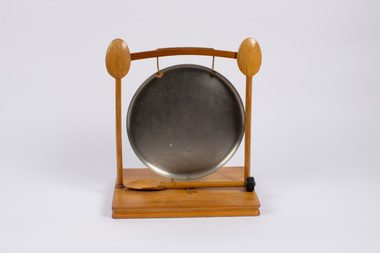 Front of dinner gong with striker (wooden spoon) attached on the stand in front of the gong.