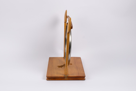 Side view of dinner gong attached to wooden stand.