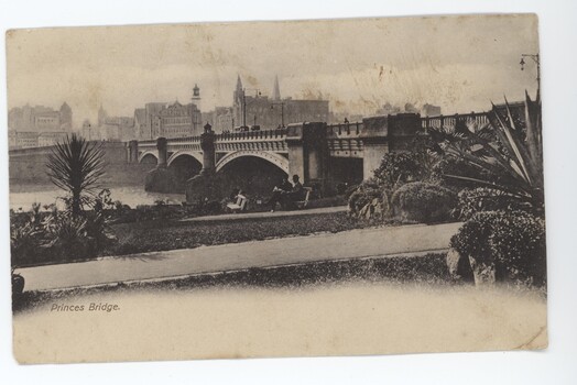 Postcard in yellowing monochrome depicting a large arch bridge spanning over water with buildings in background. Two men sitting on bench in front of bridge