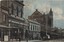 A row of early 1900s buildings along a street. There is a clocktower towards the end of the row and people walking along the footpath.