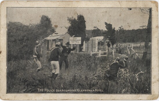 A postcard depicting four men in 1800s police uniform surrounding a white building, while a man in a suit stands in front of him with his hands up. 