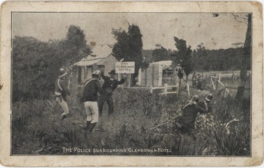 A postcard depicting four men in 1800s police uniform surrounding a white building, while a man in a suit stands in front of him with his hands up. 