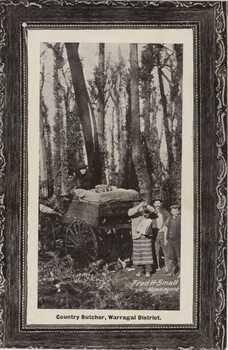 Postcard depicting black and white image of three people holding up a piece of meat for the camera, in front of a wagon being driven by a man in a dark suit in the forest.