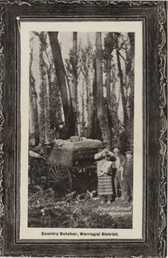 Postcard depicting black and white image of three people holding up a piece of meat for the camera, in front of a wagon being driven by a man in a dark suit in the forest.