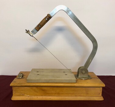 Cheese slicer on wooden base with raised arm showing cutting wire