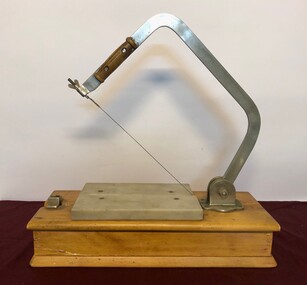 Cheese slicer on wooden base with raised arm showing cutting wire