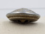 Sideview of silver button resting on a pillow, the top of it is convex, and the bottom has a raised section displaying two holes.