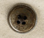 Image of underside of silver button with four holes and engraved text.