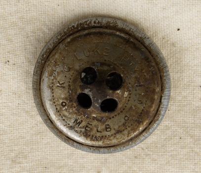 Image of underside of silver button with four holes and engraved text.