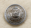 Image of top of silver button with embossed crown and text.