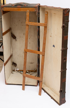 Steamer trunk open and in vertical position with hanger leaning against it