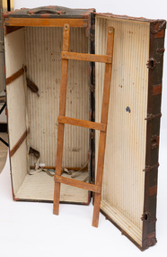 Steamer trunk open and in vertical position with hanger leaning against it