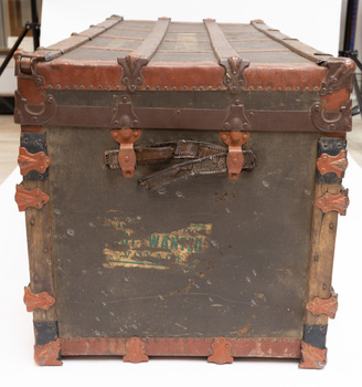 One end of steamer trunk in horizontal position showing carry strap.