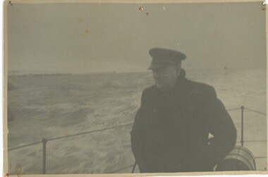 Black and white photograph of Winston Churchill aboard navy boat with ocean in background.