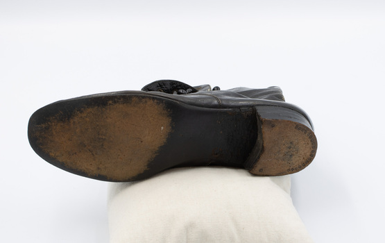 The Image shows the sole of the left shoe from a pair of black button-up boots. There is a faint engraved 3/E on the instep and a series of studs around the heel.