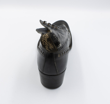 A single black low-heeled left boot, with the back facing the camera and a tag visible.