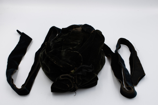 Front of black velvet hat with black velvet bow and two black ribbons for tying under the chin.