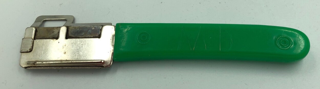 Back of bean cutter with two letters scratched into the green plastic handle.