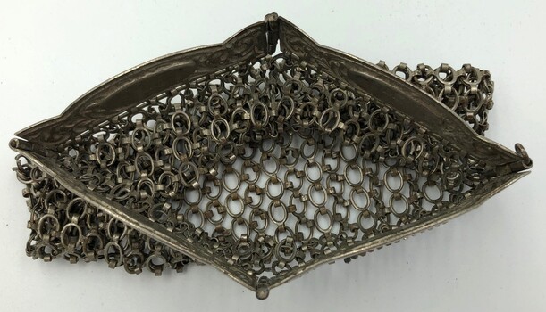 Top view of open silver chainmail evening bag showing clutch-style handle with four jointed parts.