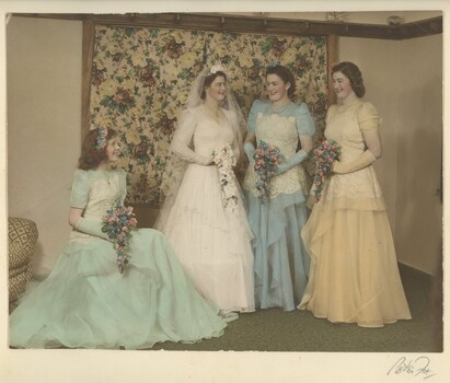 Bride with three bridesmaids, one seated and two standing with the bride all carrying posies. Two bridemaids are dressed in blue and one in yellow.