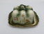 Ceramic cheese cover and plate with ornate design in green and white with gold highlights and floral decoration around all sides.