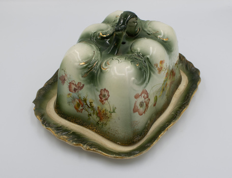 Side view of ceramic cheese cover and plate showing floral design on long end and short end.