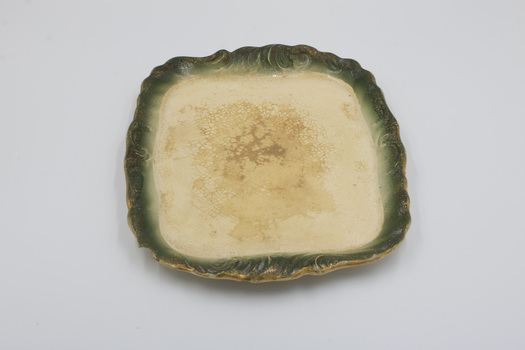 Side view of rectangular cream-colored plate with decorative green edging with gold rim.