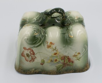 Long side of rectangular ceramic cheese plate with floral design on side and handle on top.