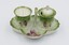 Ceramic cruet set decorated with red flowers on green and white background with pepper dispenser and salt cellar.