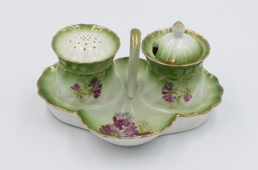 Ceramic cruet set decorated with red flowers on green and white background with pepper dispenser and salt cellar.