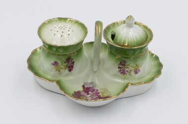 Ceramic cruet set decorated with red flowers on green and white background with pepper dispenser and salt cellar.