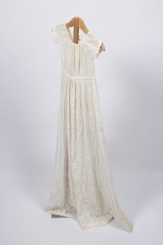 Side view of long, cream-colored christening gown on a stand