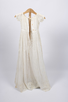 Back view of long, cream-colored christening gown on a stand with ties visible