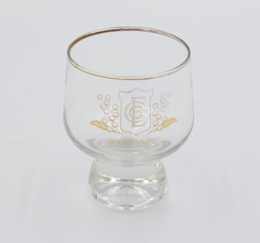 Short-stemmed, gold-rimmed drinking glass with ECC logo on the front.