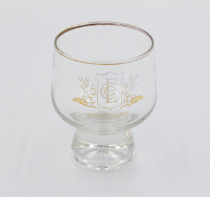 Short-stemmed, gold-rimmed drinking glass with ECC logo on the front.