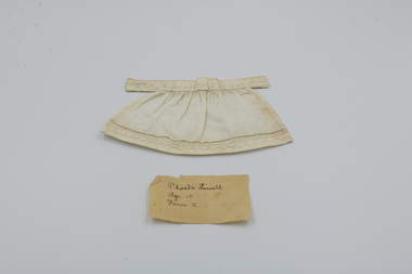 Small doll's apron hand-made by Phoebe Lewell with her original hand-written label.