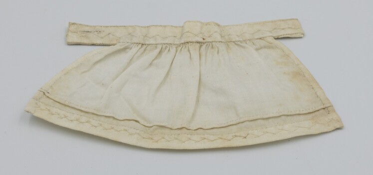 Doll's apron laid flat with decorative stitching visible.