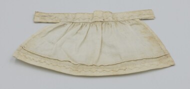Doll's apron laid flat with decorative stitching visible.