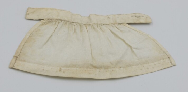 Back view of cream-colored doll's apron laid flat.