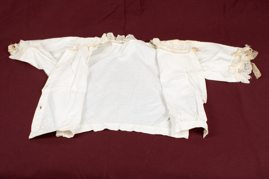 Child's lace trimmed, cream-colored blouse laid flat and opened at the front.