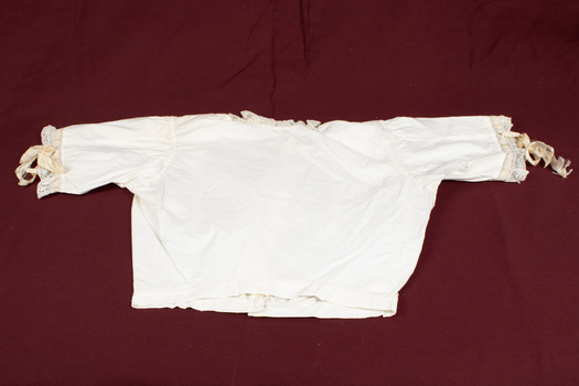 Child's blouse laid flat. Cream-colored with lace trim at sleeves and neck.