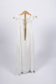 Back view of christening gown hung from wooden hanger with back tie visible