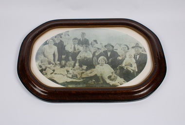 This is a framed photograph of a large family group enjoying themselves and seated together at a School picnic that was held during an Emerald Primary School outing in Mordialloc, Victoria.