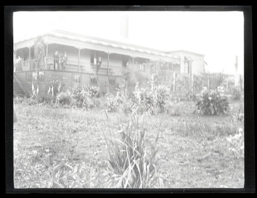 Black and white landscape view photograph of a side and back view of the Ranges Hotel, Gembrook with three men in suits and a woman standing on the balcony.