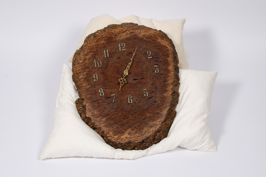 Front of analogue wood clock - oval shape with brass numbers and brass clock hands.