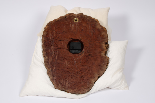 Back of carved wood clock showing brass nail holder at the top and central battery holder