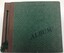 Front cover of postcard album. Embossed green. Brown leather binding with green cord.