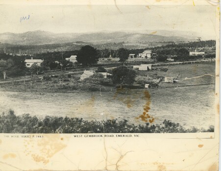 A black and white postcard featuring a road with background hills and foreground fields.