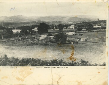 A black and white postcard featuring a road with background hills and foreground fields.